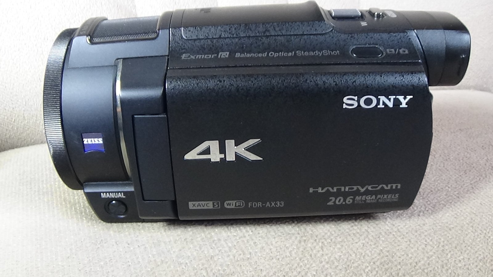Filmadora Sony FDR-AX33 compacta com a tela LCD fechada, exibindo o corpo preto fosco e o anel de controle manual na lente ZEISS.